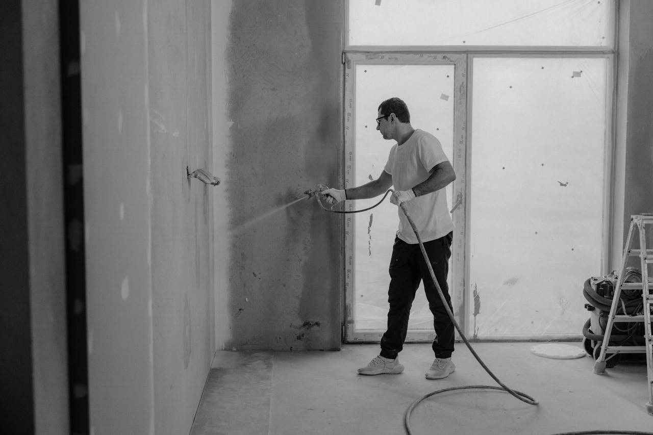 Nos Services A worker paints an interior wall with a spray gun during a renovation project.